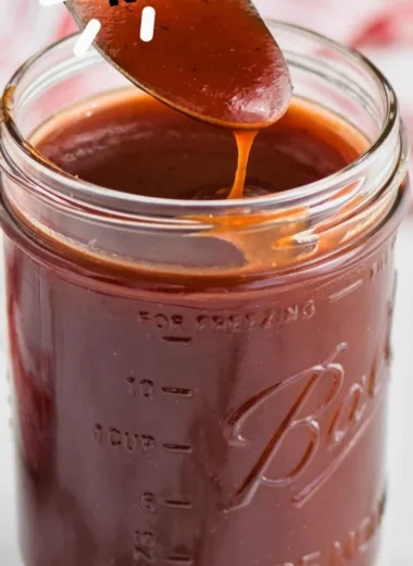 Homemade BBQ sauce in a jar with fresh ingredients on a wooden table.