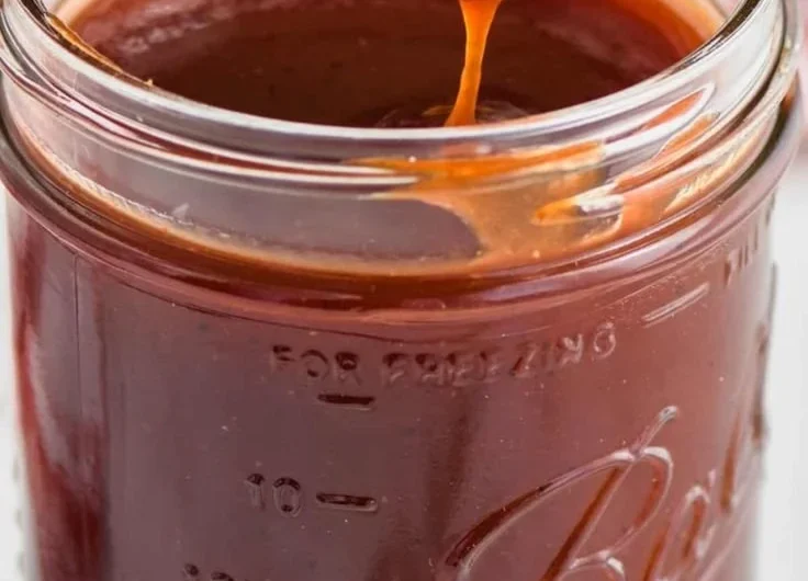 Homemade BBQ sauce in a jar with fresh ingredients on a wooden table.