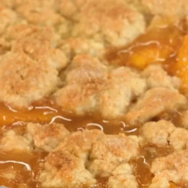 Delicious peach cobbler served in a rustic dish with fresh peaches and creamy topping.