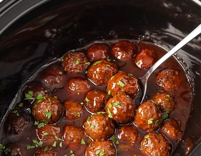 Slow cooker bourbon meatballs served in a bowl with sauce and herbs.