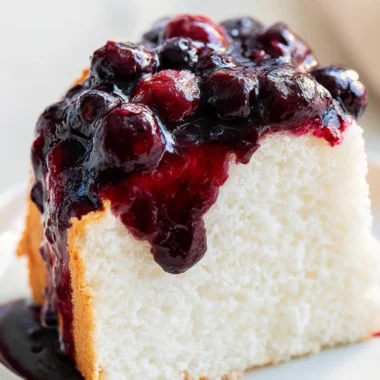 A slice of fluffy Angel Food Cake on a white plate topped with fresh berries