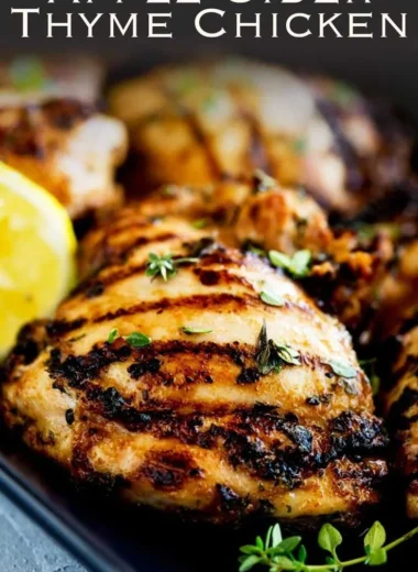 Grilled apple cider thyme chicken on a plate garnished with herbs.
