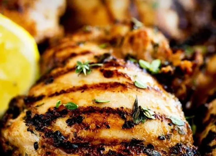 Grilled apple cider thyme chicken on a plate garnished with herbs.