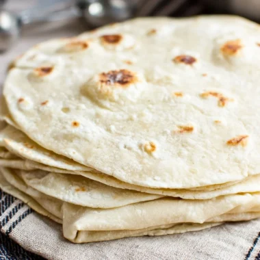 Homemade flour tortillas stacked on a wooden table ready for use.