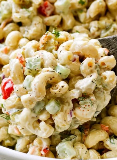 Delicious macaroni salad in a serving bowl with fresh vegetables and dressing