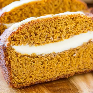 Loaf of cozy pumpkin bread with cream cheese frosting on a wooden cutting board