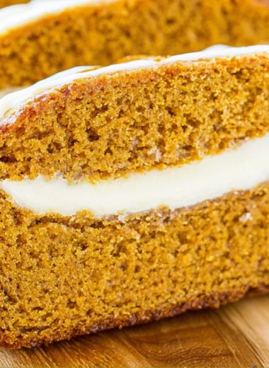 Loaf of cozy pumpkin bread with cream cheese frosting on a wooden cutting board
