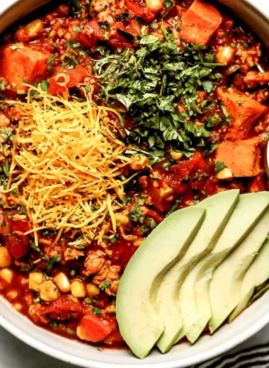 Bowl of sweet potato turkey chili garnished with herbs and avocado